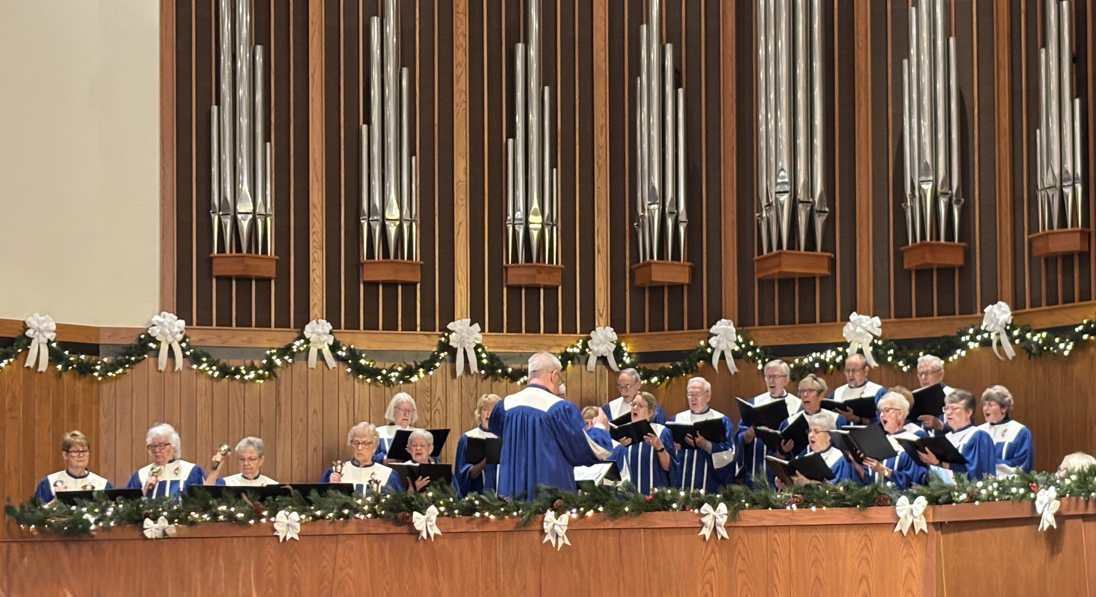 Choir performs in front of a large pipe organ in a grand hall.