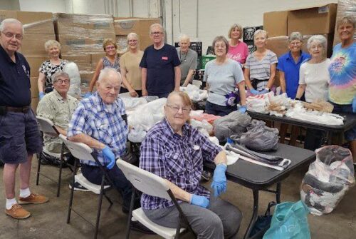 A group of elderly people gathered indoors, smiling and seated around a table.