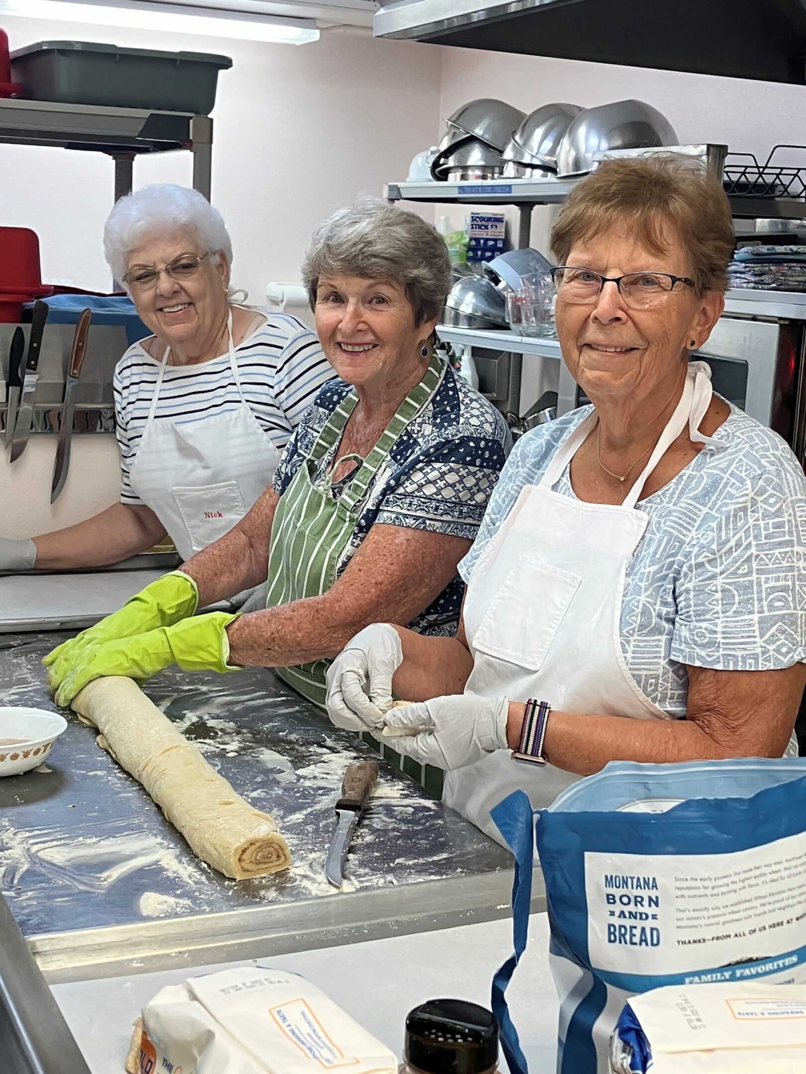 Three elderly women baking together in a kitchen.