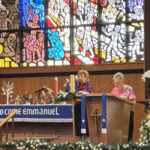 A priest and a woman at a church altar with stained glass windows.