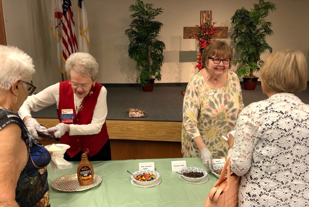 Two women serve food at a community event in a decorated hall.