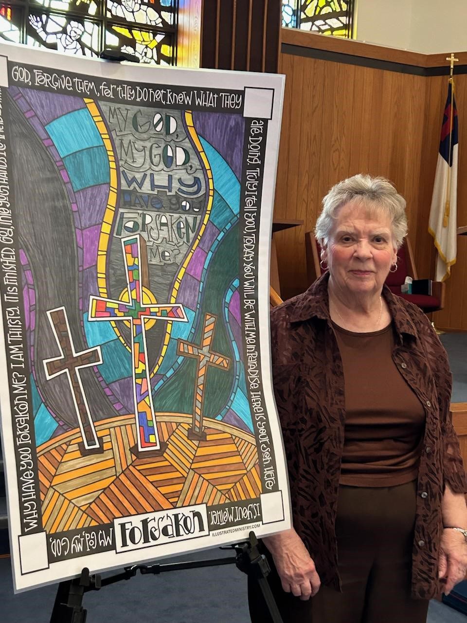 Woman standing next to a colorful artwork featuring three crosses and abstract shapes.