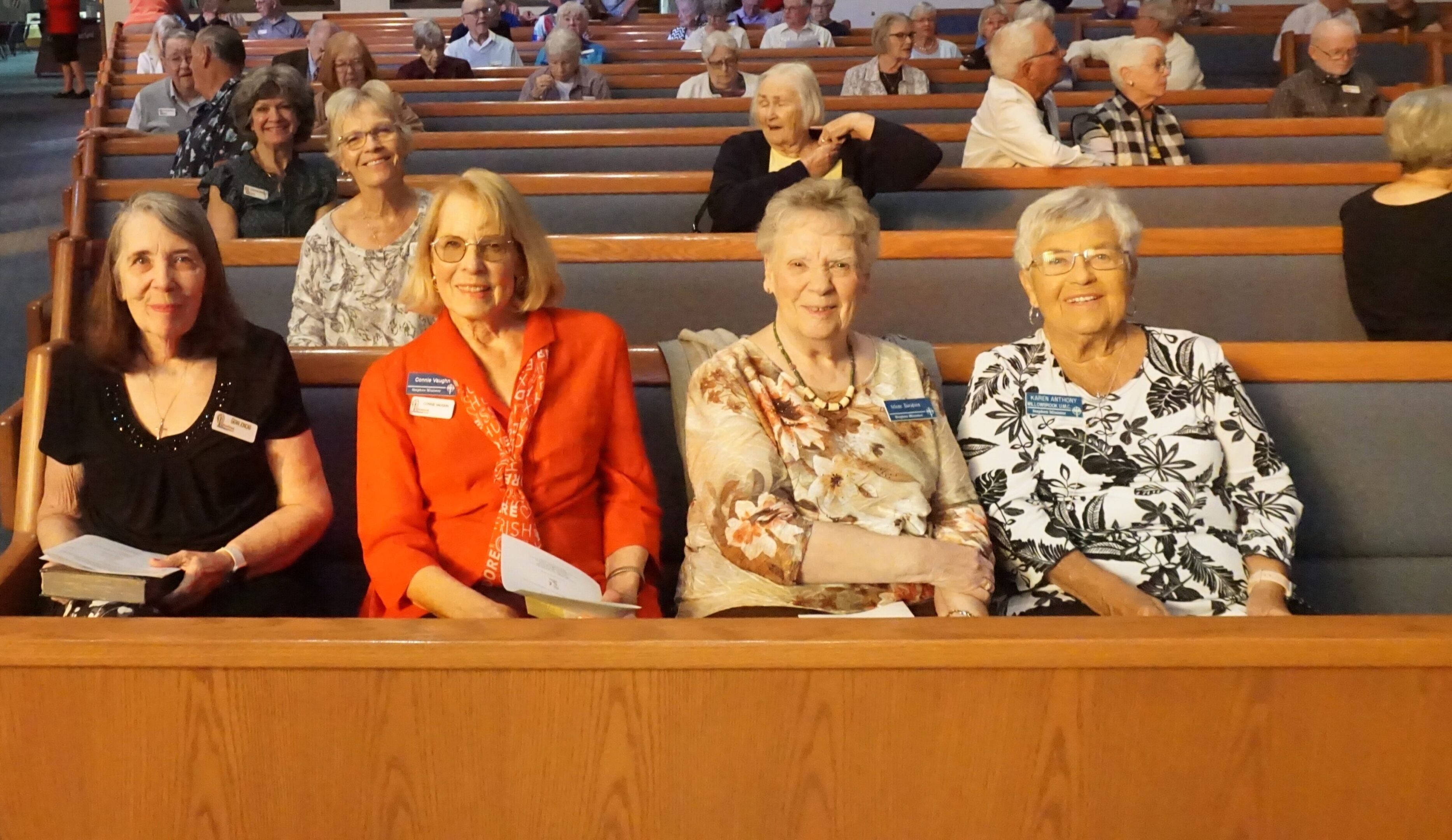 Three elderly women seated in a church pew, smiling towards the camera.