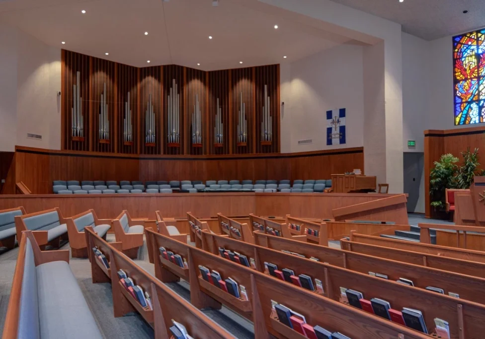 Empty wooden pews inside a church sanctuary with an organ in the background.